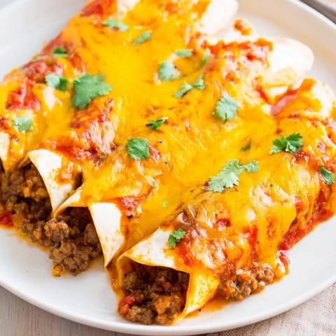 A close-up of a baking dish full of hot, cheesy Beef Enchiladas, ready to be devoured.