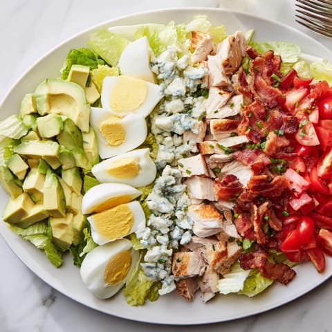 Freshly prepared Cobb Salad with juicy tomatoes, hard-boiled eggs, and a tangy vinaigrette dressing.