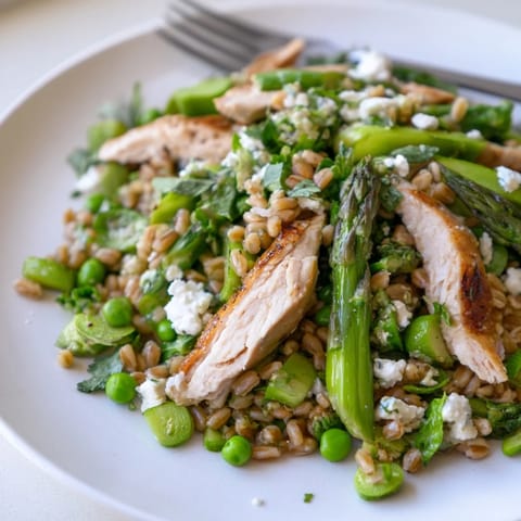 Overhead view of a vibrant Warm Spring Farro Chicken Salad in a white bowl, featuring feta crumbles and fresh herbs, ready for a light lunch or dinner.