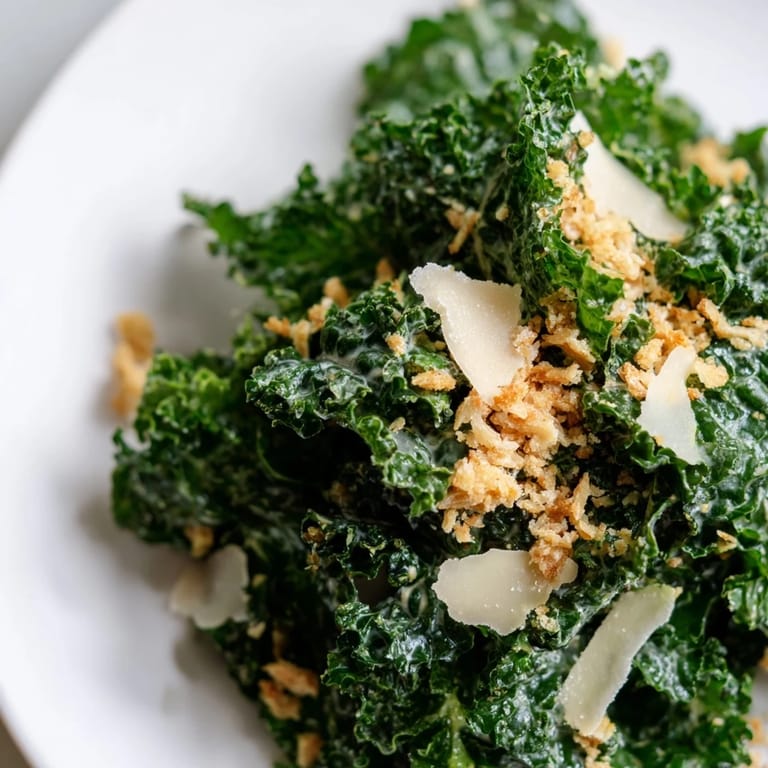 Garlic Parmesan Kale Salad with tender massaged kale leaves, a creamy garlic-Parmesan sauce, and crunchy toasted breadcrumbs, garnished with freshly cracked black pepper.