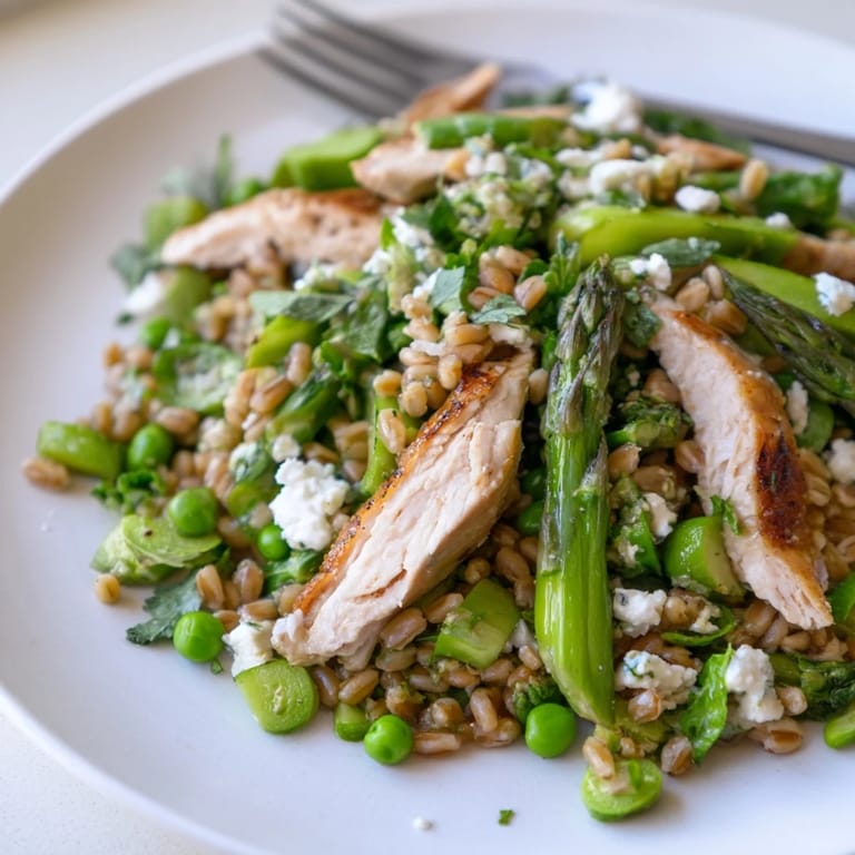 Overhead view of a vibrant Warm Spring Farro Chicken Salad in a white bowl, featuring feta crumbles and fresh herbs, ready for a light lunch or dinner.