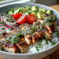 Freshly grilled chimichurri chicken slices rest atop fluffy rice with avocado and cherry tomatoes.