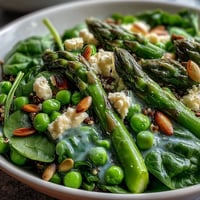 Bright Spring Green Bowl topped with blanched asparagus, peas, and green beans on quinoa, drizzled with lemon dressing. 