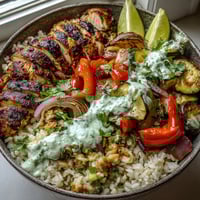 Golden-brown blackened chicken breast sliced over fluffy white rice, with sautéed bell peppers and zucchini topped with creamy lime crema.