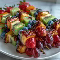 Rainbow Fruit Skewers with Honey Dip: A colorful arrangement of fresh strawberries, pineapple, kiwi, blueberries, grapes, and cantaloupe on skewers, served with a creamy honey-yogurt dip for a refreshing snack.